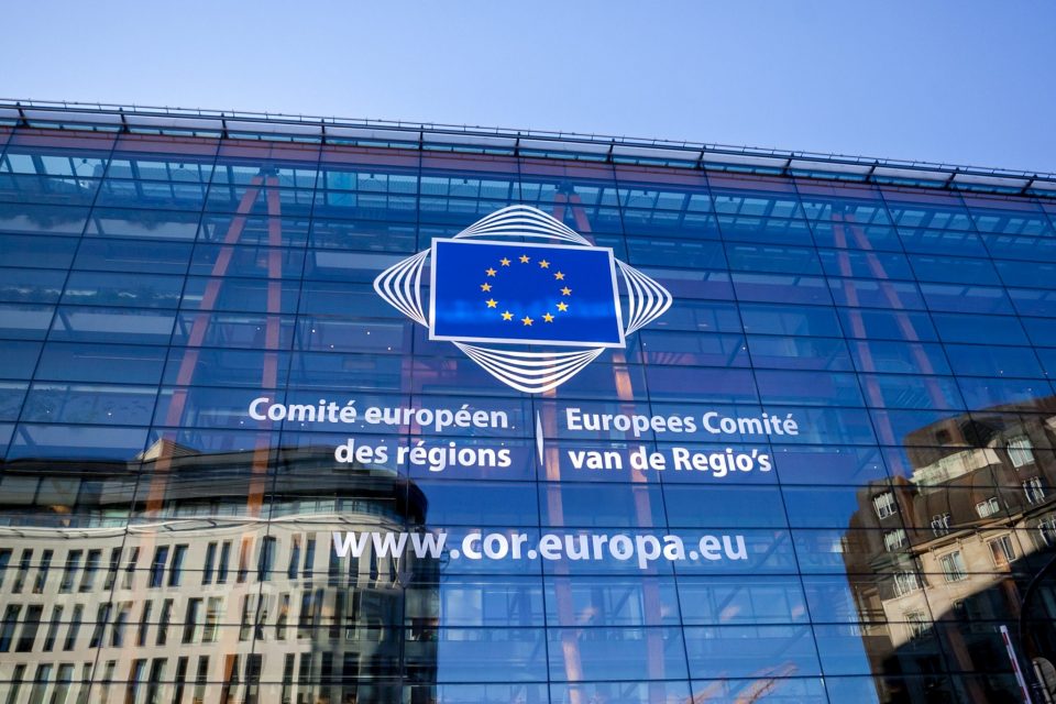 Das Bild zeigt das gläserne Gebäude des Ausschuss der Regionen. Mittig ist die Flagge der EU auf dem Gebäude zu sehen.